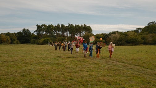 A group of people dressed in bright colours parade across an open plain at Hatfield Forest